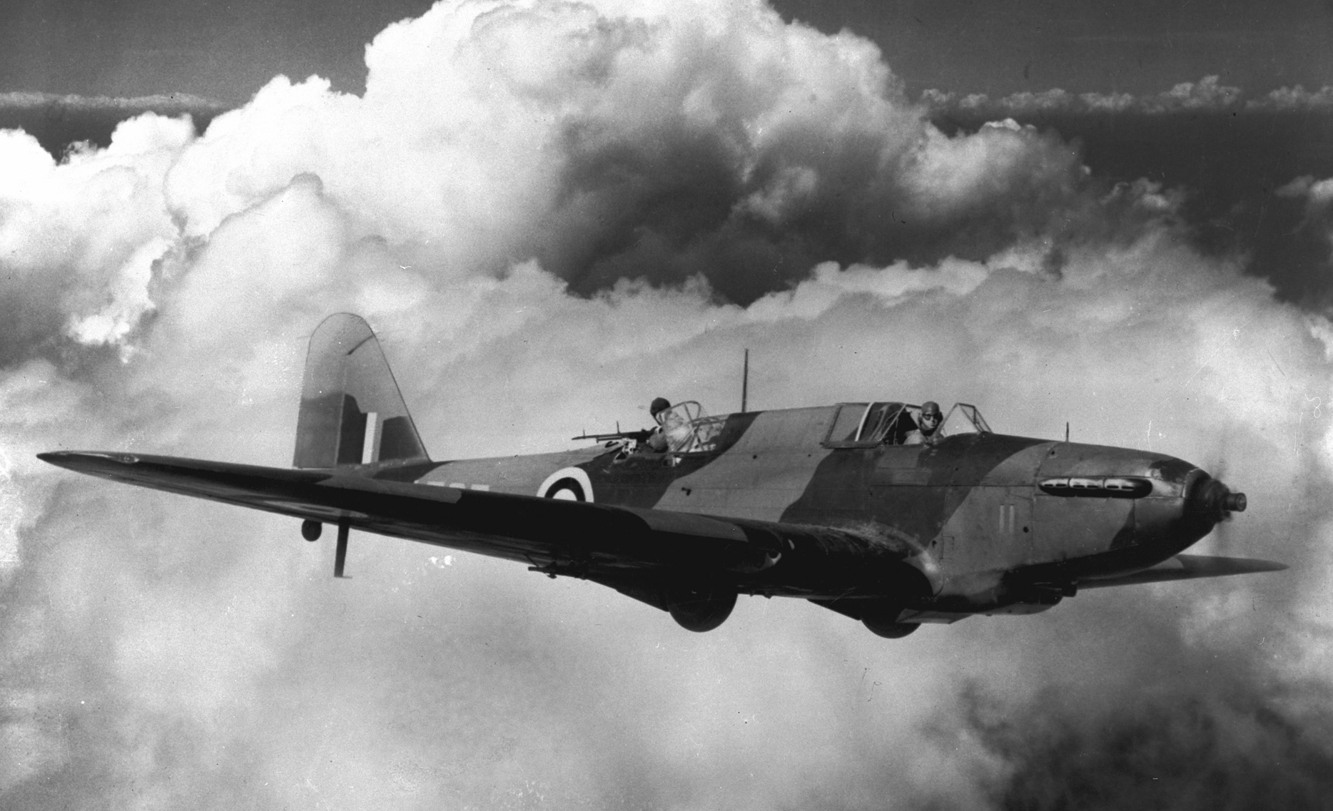 La légende de cette photo se lit comme suit : « Se découpant sur des nuages, un bombardier-école Fairey Battle effectue un vol près d’une station de l’Aviation royale canadienne au Canada. Bien qu’aujourd’hui désuète à titre d’appareil de combat, cette variante utilisée aux écoles de bombardement et de tir s’est montrée utile à Dunkirk. » PHOTO : Archives du MDN, PL-3039 